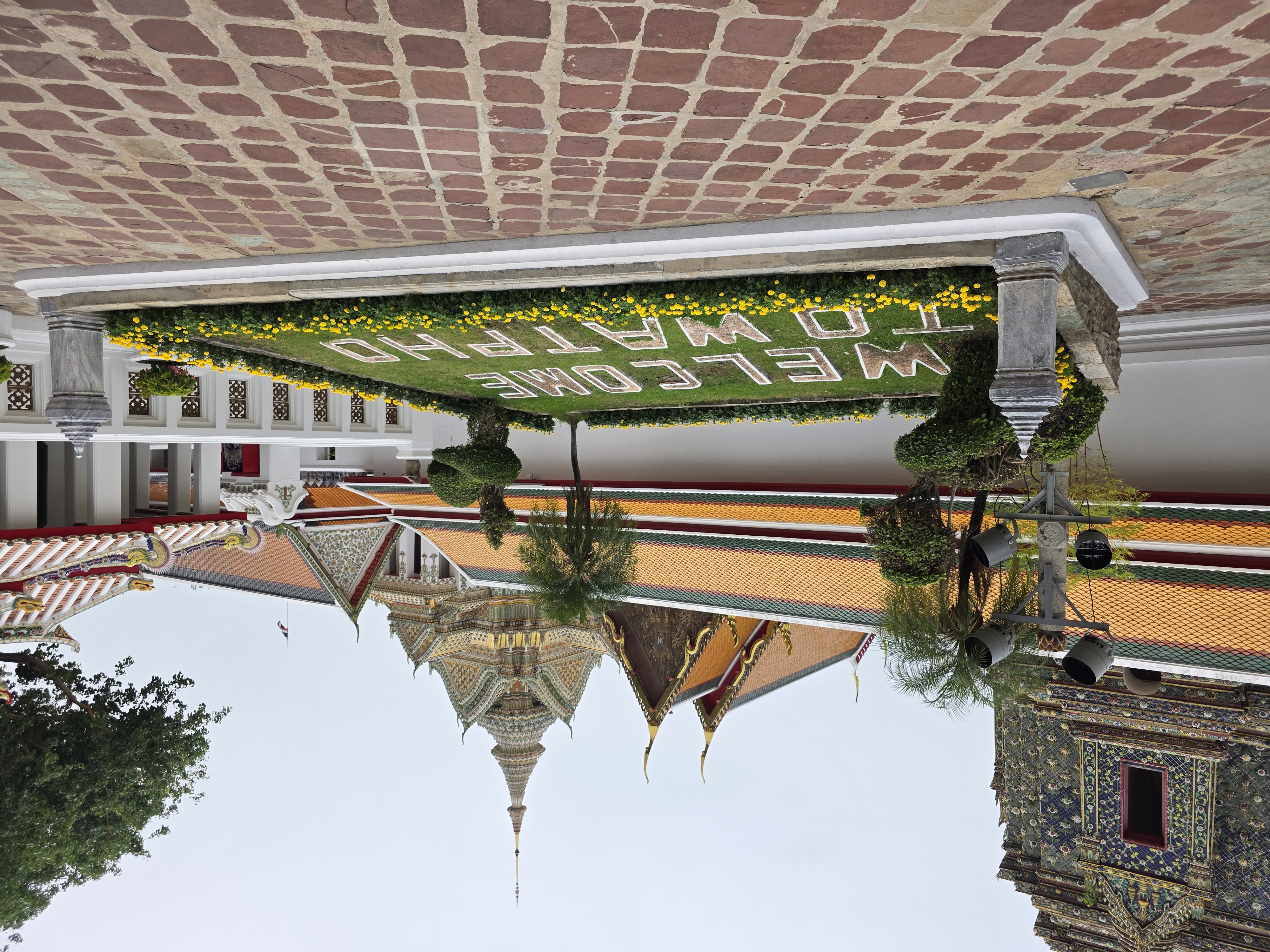 "Welcome to Wat Pho" topiary sign, temple spires