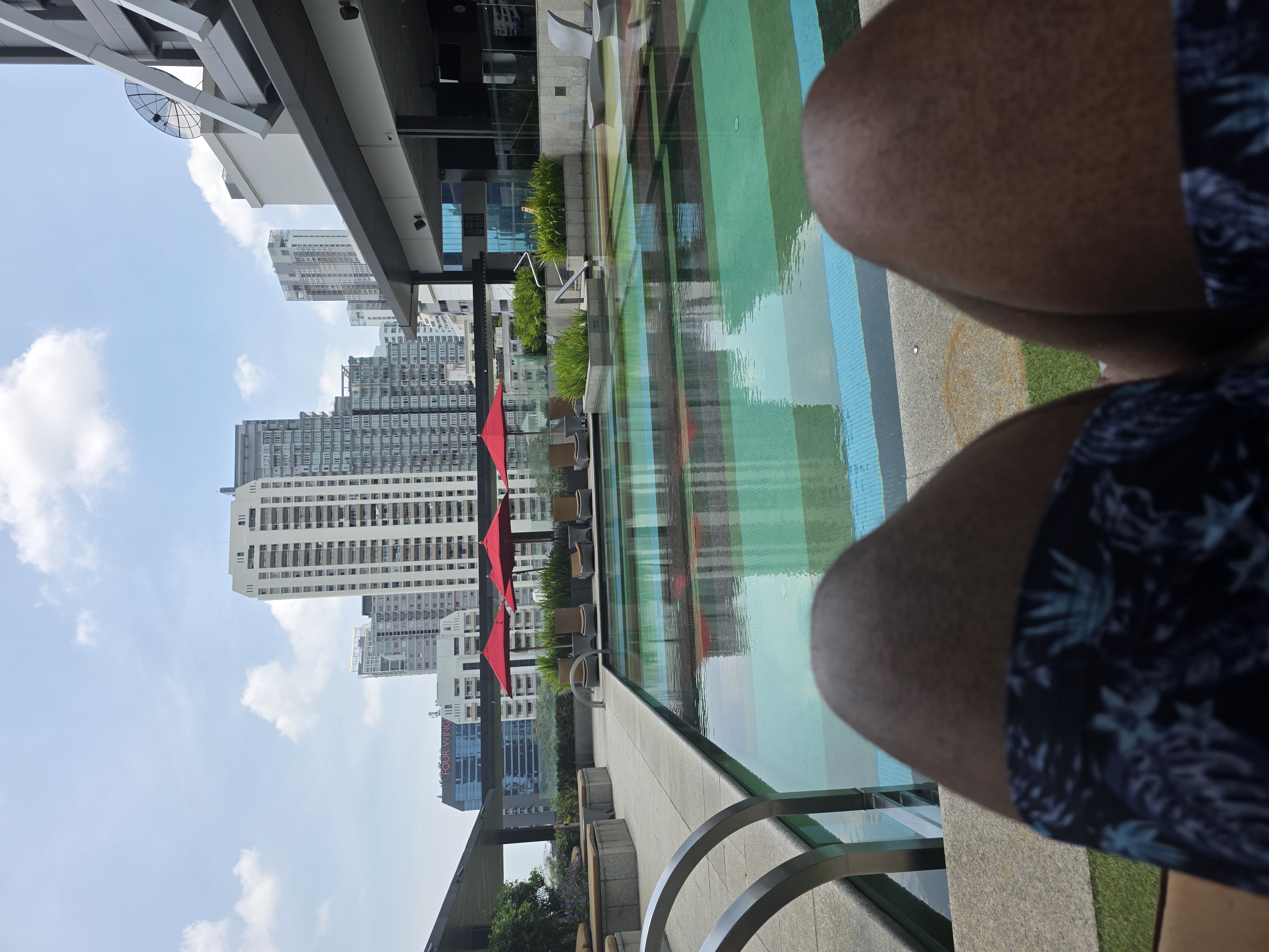 rooftop hotel pool, Rodney's legs in foreground, city skyline behind