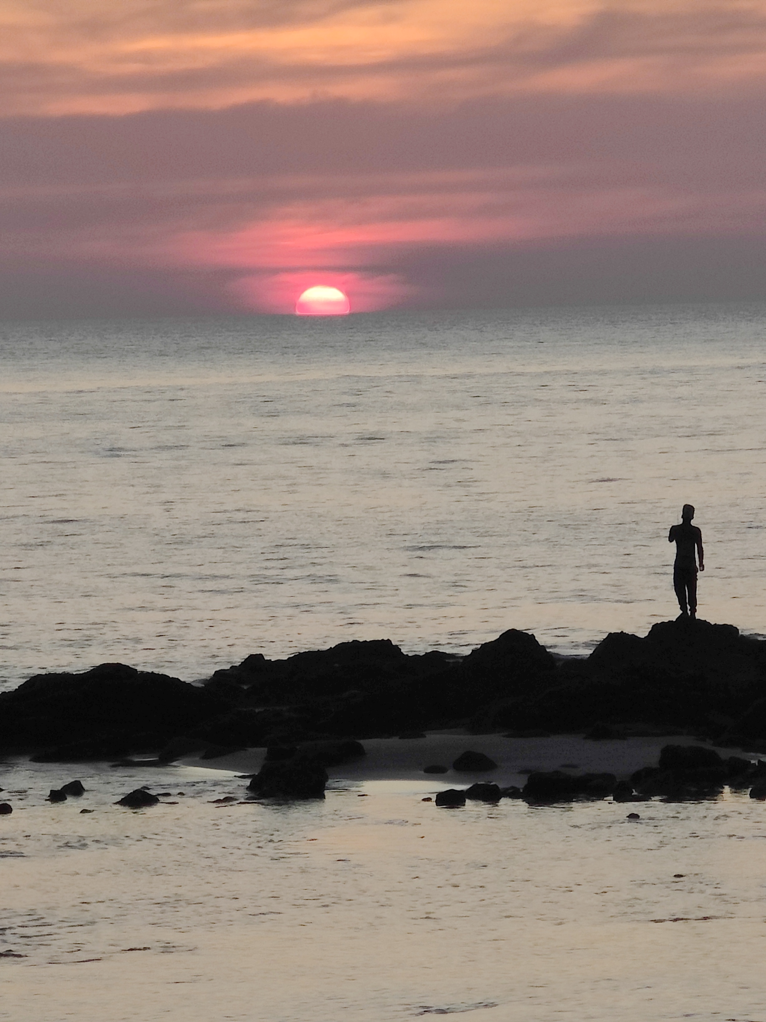 silhouetted figure on rocks watching pink sunset